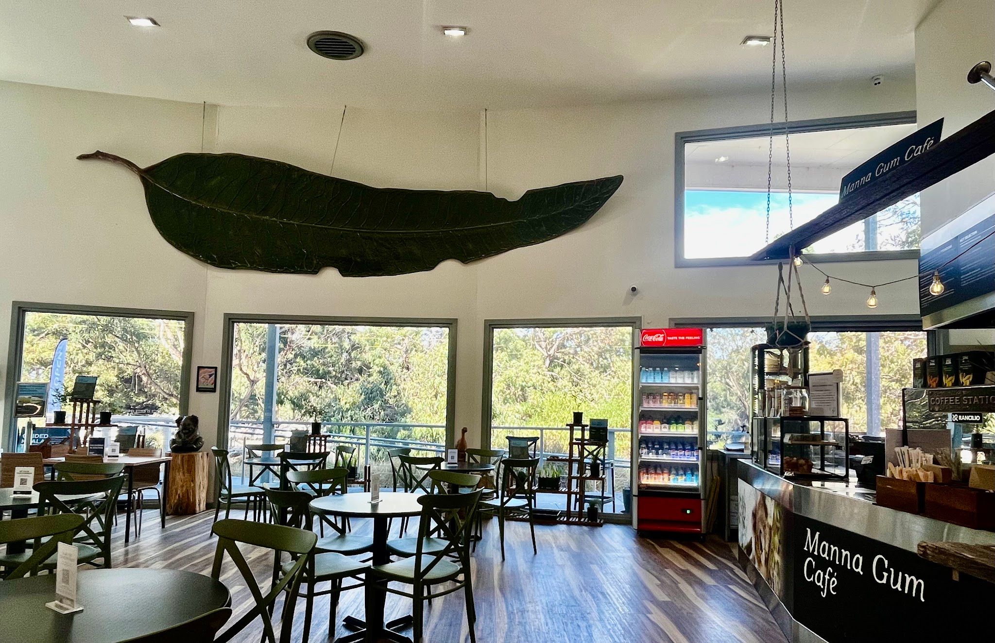 Bright interior of Manna Gum Cafe with large leaf sculpture above dining room and bush views through windows